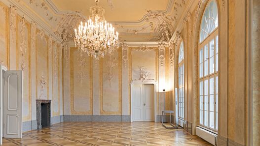 Blick in einen mit Stuck verzierten Saal mit Kronleuchter im Schloss Schönhausen