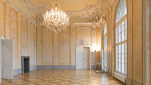 Blick in einen mit Stuck verzierten Saal mit Kronleuchter im Schloss Schönhausen