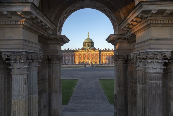 Blick durch die Kolonnaden auf das im Abendlich leuchtende neue Palais im Park Sanssouci