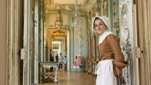 Kammerzofe Sophie lädt ins Schloss Charlottenburg © SPSG / Peter Adamik Eine als Kammerzofe verkleidete junge Frau steht an einer geöffneten Tür, hinter ihr ist Schlossraum zu sehen