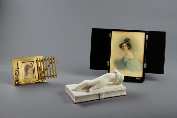 Drei Erinnerungsstücke: Porträtfotografie Augusta Hand auf einem Buch liegend, Porträt Elisa Radziwill © SPSG / Daniel Lindner Drei Erinnerungsstücke: Porträtfotografie der Prinzessin/Königin Augusta im Rahmen in Form eines Gartentors: "THE GARDEN GATE", Johann von Halbig: Hand auf einem Buch liegend, Ludwig Sebbers: Porträt Elisa Radziwill im Klapprahmen