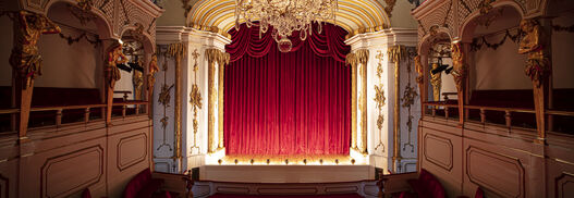 Schlosstheater im Neuen Palais von Sanssouci, schräger Blick zur Bühne mit geschlossenem Vorhang, bei abgedunkeltem Licht