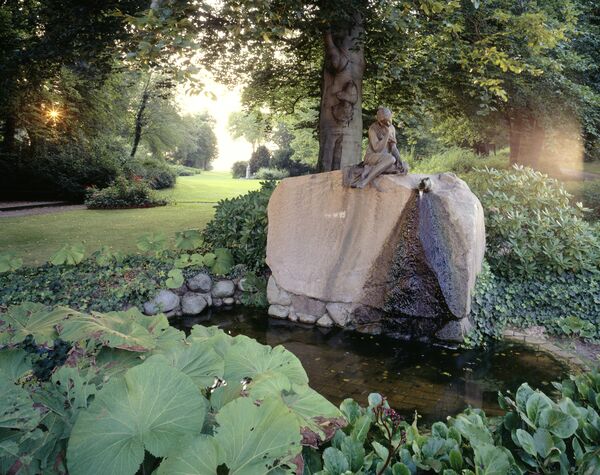 Die Skulptur "Das Trauerende Milchmädchen" im Park Glienicke inmitten von Pflanzen in einem kleinen Teich