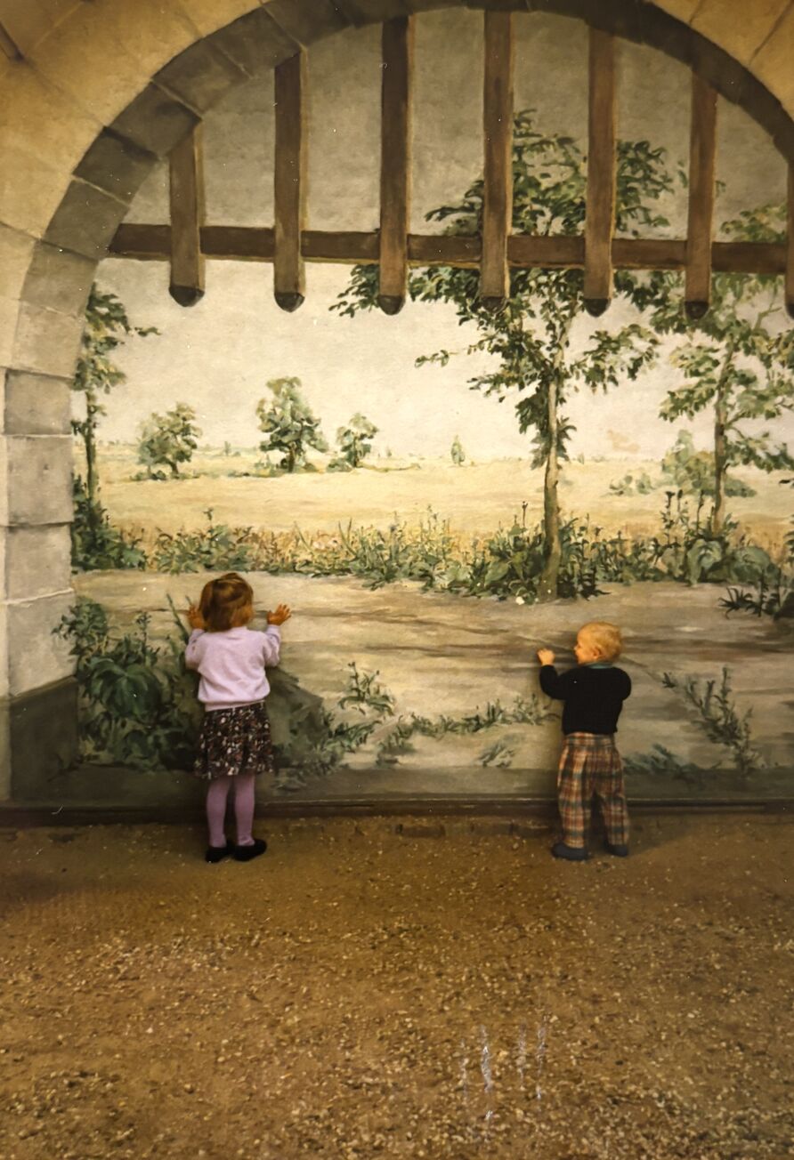 Zwei Kinder stehen am Wandbild in der Bogennische des Schlosses Pfaueninsel und schauen in die fiktive Landschaft 