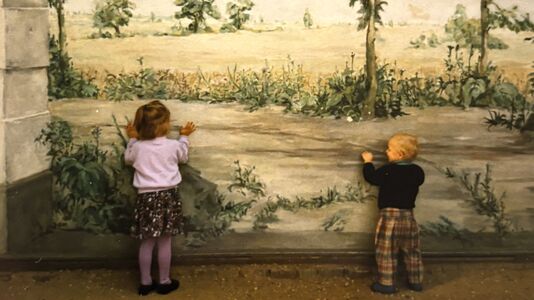 Zwei Kinder stehen am Wandbild in der Bogennische des Schlosses Pfaueninsel und schauen in die fiktive Landschaft 