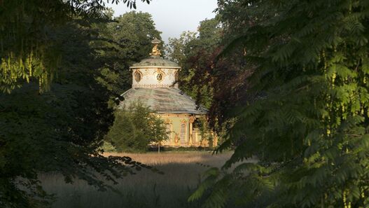 Blick durch grüne Blätter über den Parkgraben auf das Chinesische Haus im Park Sanssouci