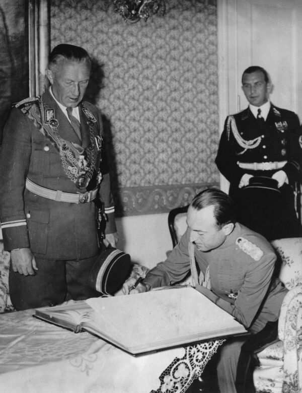 In the presence of Lord Mayor Julius Lippert (links), Prince Regent Paul of Yugoslavia (seated) enters his name in the “Golden Book” of the city of Berlin at Bellevue Palace, the guesthouse of the government of the German Reich. In the background is Municipal Director Walter Rummert, June 1939