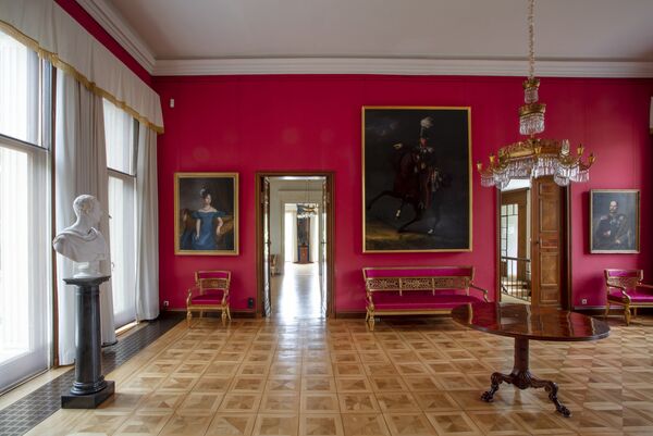 Blick in den Roten Salon im Schloss Glienicke, mit roten Wänden, Parkett und Gemälden 