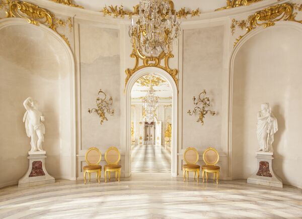 Blick in den weißen Buffetsaal mit goldenen Wandverzierungen und goldenen Stühlen in den Neuen Kammern von Sanssouci