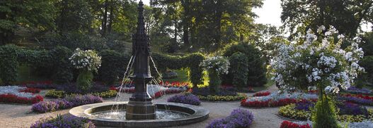 Blick in den Gotischen Garten mit bunt blühenden Blumenbeeten und Fontäne im Park Babelsberg