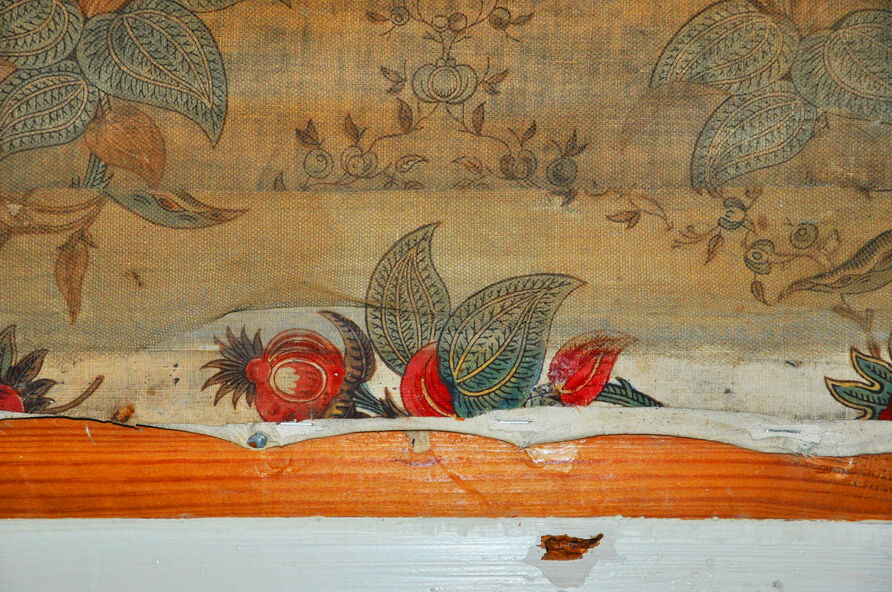 Unter einer Holzleiste wartete eine Überraschung auf die Textilrestauratorinnen: die kraftvolle rote, grüne, blaue und violette Farbigkeit der mit üppigen Blüten, Blättern und kleinen Vögeln bedruckten weißen Baumwolle war noch erhalten