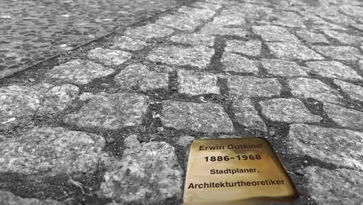 „Übergangene Steine“, Ausstellung über Erwin Gutkind im Schloss Schönhausen, Plakatmotiv mit eingepflasterten Stolperstein in Vordergrund und Silhoutten von Menschen, die darübergehen