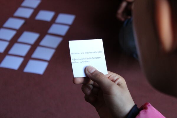 Kinderhand mit Zettel: Ein rätselhafter Spruch des Memory-Spiels – Angebot für Schulen im Jagdschloss Grunewald