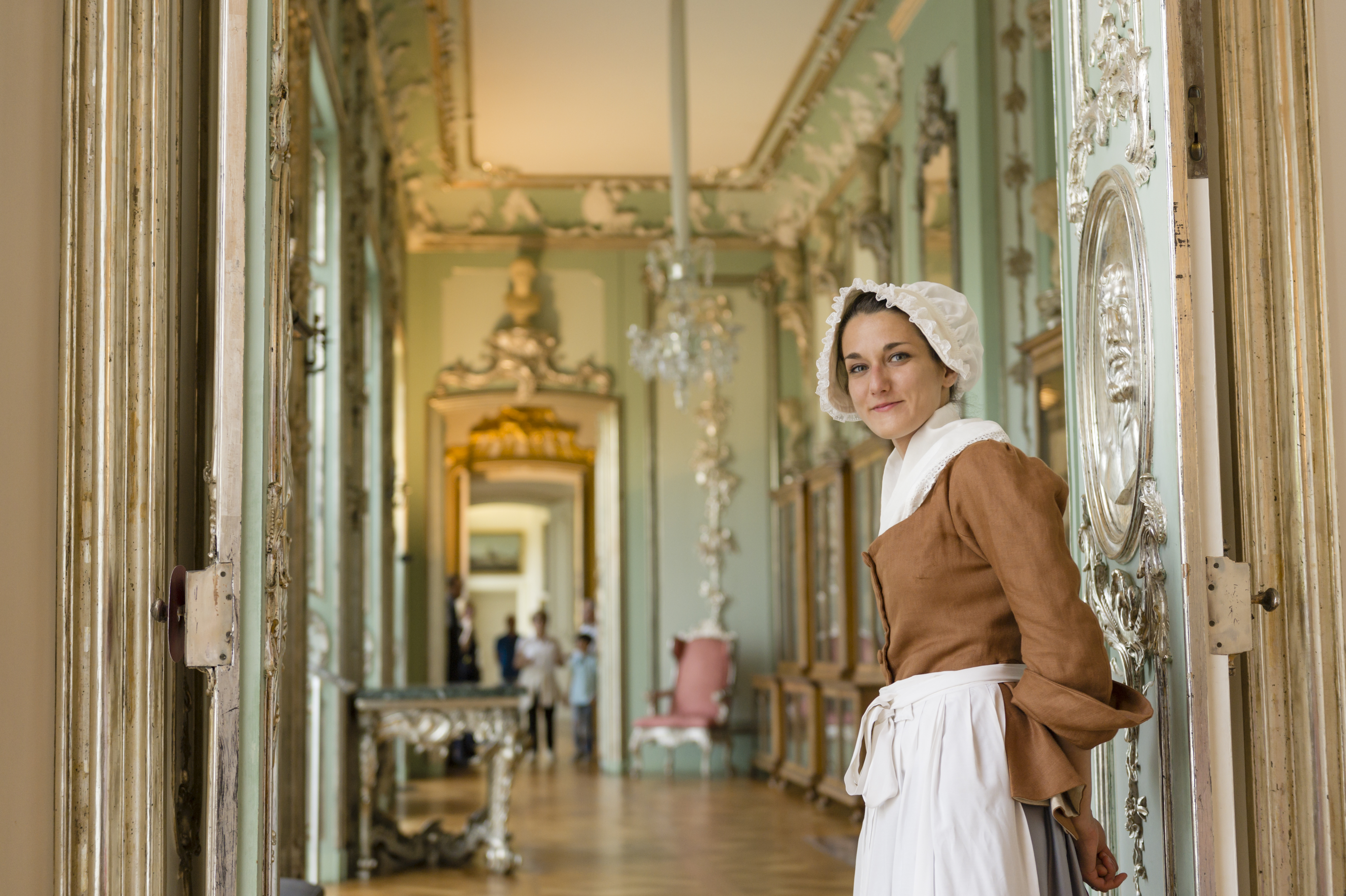 Eine als Kammerzofe verkleidete junge Frau steht an einer geöffneten Tür, hinter ihr ist Schlossraum zu sehen